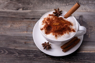 Pumpkin Spice Latte pumpkin drink topped with whipped cream sits in a white cup. Surrounding it pumpkins and cinnamon sticks creating a festive fall atmosphere.