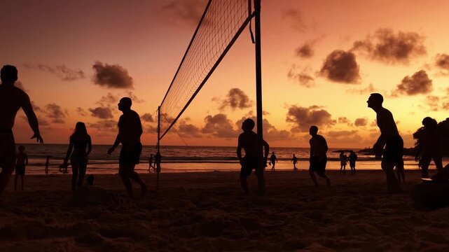 Young people playing beach volleyball by the ocean at sunset