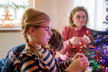 Little school girl, teenager boy and mother decorate traditional Christmas tree with vintage decorations and toys at home