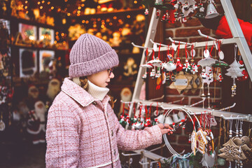 Little school girl on Christmas market. Child in a shop with Christmas tree decorations and Santa...