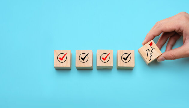 Success building concept with hand stacking wooden blocks step by step, showing checkmarks and progress icons, representing achievement, planning, strategy, and long-term development.