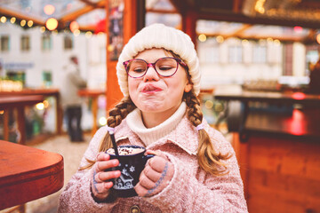 Little cute preschool girl drinking hot children punch or chocolate on German Christmas market. Happy child on traditional family market in Germany,