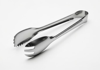 Obraz premium Shiny metal serving tongs rest diagonally on a bright white surface.