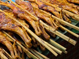 Close-up of golden-brown grilled chickens on skewers, lying on a bamboo mat for serving.