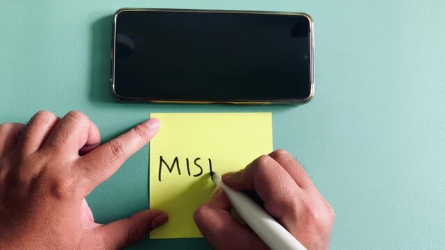 hands write mistake word on a yellow sticky note next to a smartphone, concept of smartphone addiction 