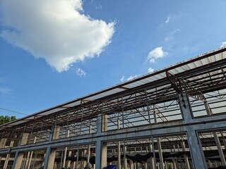 Fototapeta premium A low-angle shot of a large, open-sided metal and concrete structure with a translucent roof, set against a bright blue sky with a single white cloud.