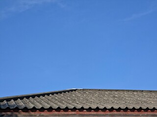 A very low-angle shot of a dark gray, wavy corrugated asbestos roof against a clear, deep blue sky.