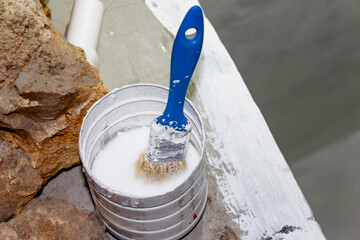 Blue-handled paintbrush soaking in cloudy white liquid inside a small plastic container