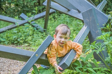 A young boy climbs on a wooden play structure surrounded by trees, embodying the spirit of adventure, exploration, and the joys of childhood learning and play
