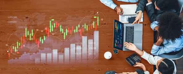 A diverse business team collaborates on financial analysis using charts and a laptop. The modern office setting promotes teamwork and strategic planning. Scalp