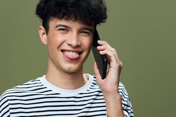 smiling man speaking on smartphone showing playful expression with tongue out, wearing striped shirt against green background, casual young male portrait