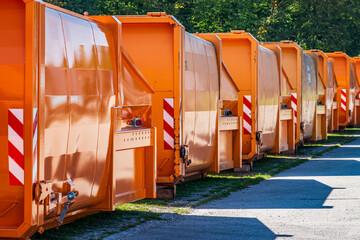Multiple orange recycling bins lined up in a neat row at a waste management facility on a clear day