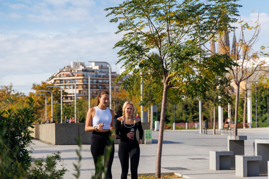 Fit women jogging side by side in a calm park wearing sporty outfits and enjoying a peaceful outdoor workout experience
