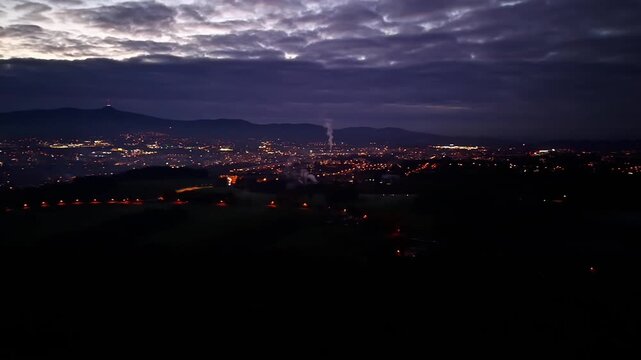 illuminated neighborhoods beneath cloudy sky, aerial view of glowing city streets and industrial