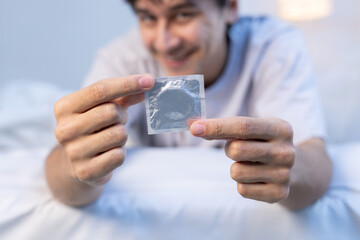 Man smiles while holding condom packet in room comfortable moment in private space.