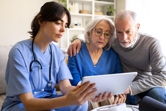 Female doctor showing information on tablet to senior couple at home visit - Powered by Adobe