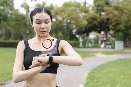 Asian women checking smartwatch with digital health data overlay, representing fitness tracking, heart rate monitoring and active lifestyle technology in an outdoor environment.