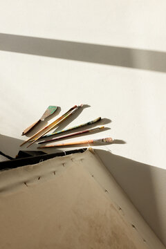 Six painting tools and canvas edge are lying on sunlit white tabletop, casting soft shadows