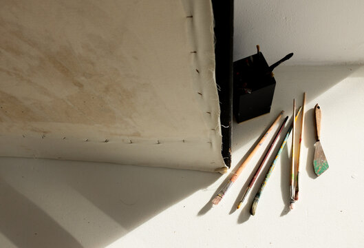Backside of stretched canvas lying on white table with fanned brushes, palette knife, brush holder