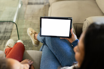 Tablet resting centered on light-colored sofa cushion near glass coffee table on patterned rug