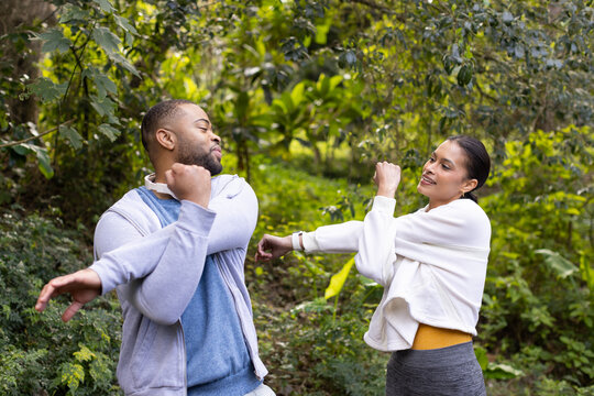 Diverse friends stretching arms across chests on wooded trail in sportswear with smartwatch