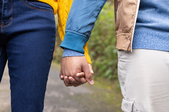 Couple walking garden path wearing yellow sweater and blue bomber jacket while holding joined hands