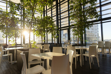 White tables and chairs are basking in low-angle sunlight at high-rise cafe, casting long shadows