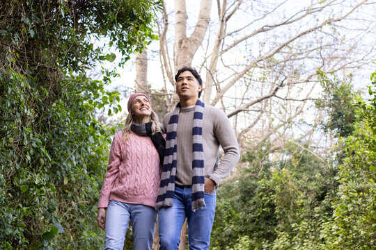 Diverse couple walking together along garden path wearing striped and knit scarves with pink beanie