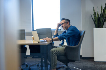 Male office worker sitting at meeting table using laptop by coffee cup and smartphone, copy space