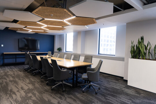 Long wooden conference table is anchoring office meeting room with gray chairs and honeycomb panels