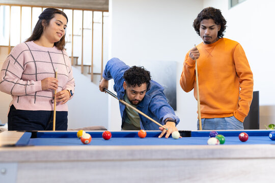 Friends playing pool with cues and scattered balls around blue-felt billiard table in home rec room