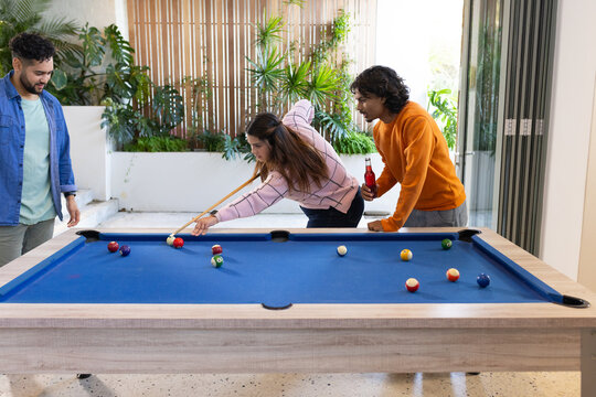 Diverse friends leaning over blue felt pool table and holding bottled beverage in home game room - Powered by Adobe
