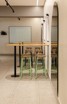 Cluster of three pale green stools sitting under wooden bar table, mirror reflecting terrazzo floor
