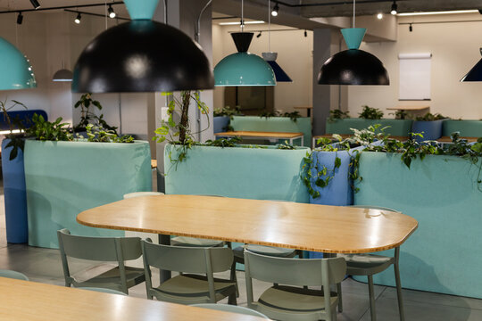 Rounded light wood communal table occupying center in office lounge with four green-gray chairs - Powered by Adobe