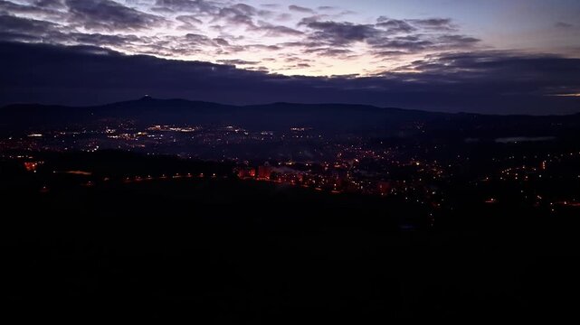 night city skyline, aerial perspective of luminous streets over mountain silhouettes during dusk