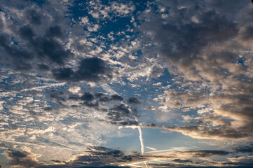 Vom Sonnenlicht angestrahlte Schicht-, Schleiher- und Sch&auml;fchenwolken mit sich kreuzenden Kondensstreifen am Abend- oder Morgenhimmel