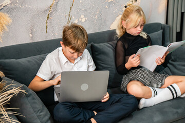 Children Laptop Couch Learning: Boy uses laptop while girl reads on couch at home.
