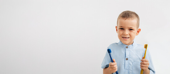 smiling boy with a natural baby tooth gap holding two colorful toothbrushes on a white background