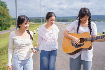 Teenage girls enjoying music together as one plays acoustic guitar while friends smile and use a smartphone, creating a joyful and creative moment.