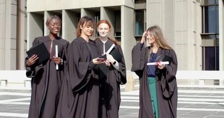 Diverse female graduates walking on plaza pulling smartphone taking selfie celebrating graduation - Powered by Adobe