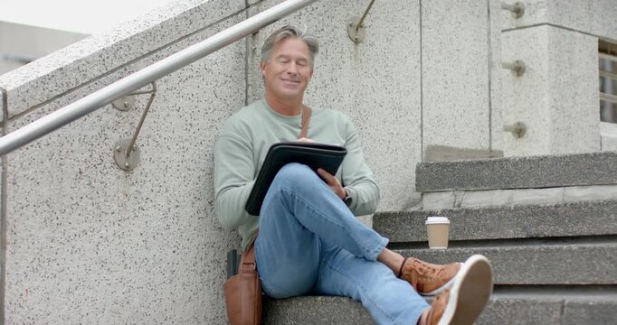 Mature adult male reaching at building steps placing coffee opening tablet scrolling content