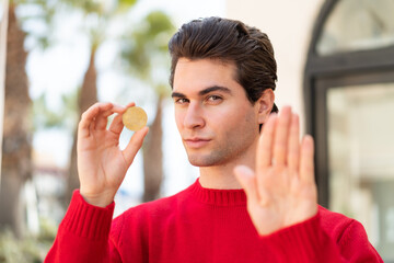 Young handsome man holding a Bitcoin and doing stop sign