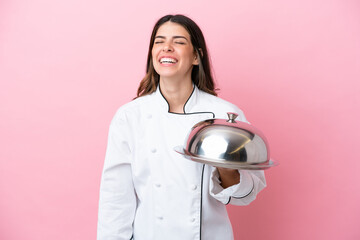 Young Italian chef woman holding tray with lid isolated on pink background laughing in lateral position
