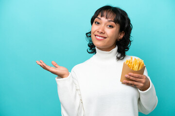 Young Argentinian woman holding fried chips isolated on blue background extending hands to the side for inviting to come