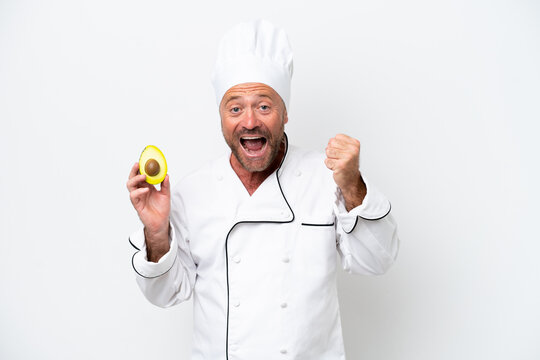 Chef man holding an avocado isolated on white background celebrating a victory in winner position