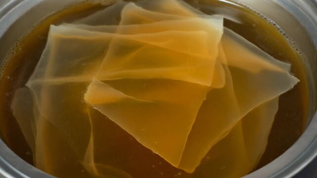 Close-up of layered, translucent, amber-hued sheets submerged in liquid within a metal container