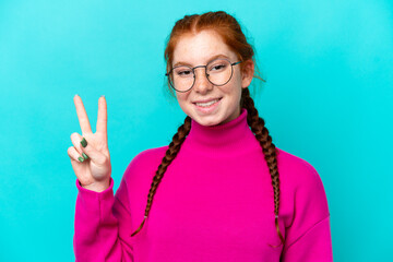 Young reddish woman isolated on blue background With glasses and doing OK sign