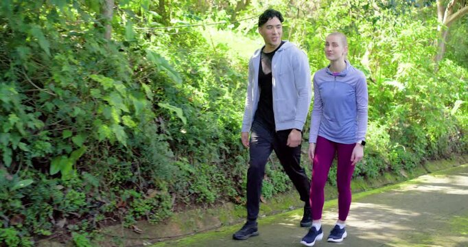 Diverse couple hiking paved forest path noticing something in trees, pointing upward, resuming hike