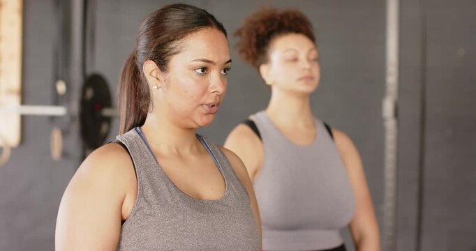 Diverse female friends gripping dumbbells and doing upright rows at gym for shoulder strength
