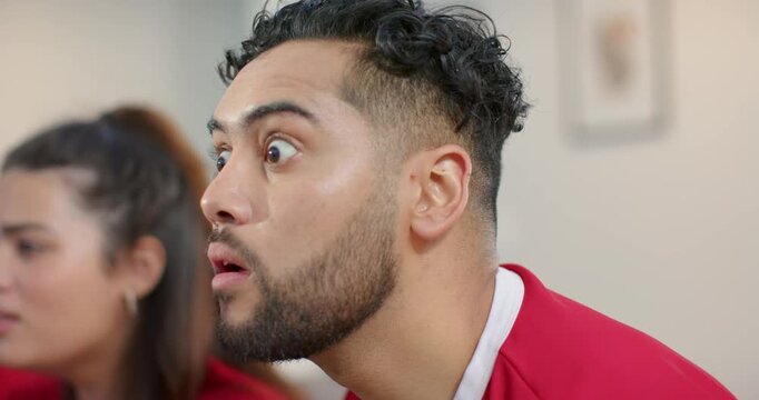 Diverse couple wearing red sports jerseys sitting on sofa at home cheering after goal, copy space
